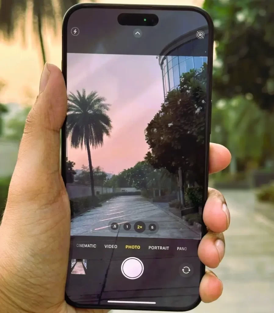 A person holding up an iPhone 15 Pro Max displaying a photo of a park, capturing the beauty of nature.