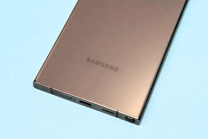 A gold Samsung S24 ultra with “SAMSUNG” engraved on the back, tilted diagonally on a light blue background.